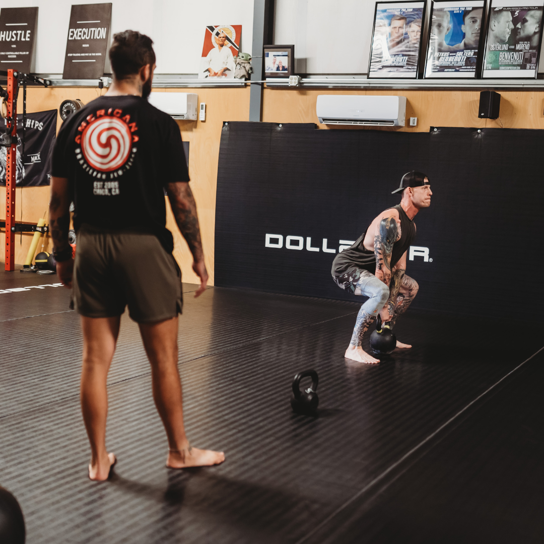 A personal coach watches a professional athlete practice kettlebell squat form during a training session, representing the expert exercise-form technique and personal coaching focus Gym Truck Chico brings to in-home and mobile workouts in Chico, CA.