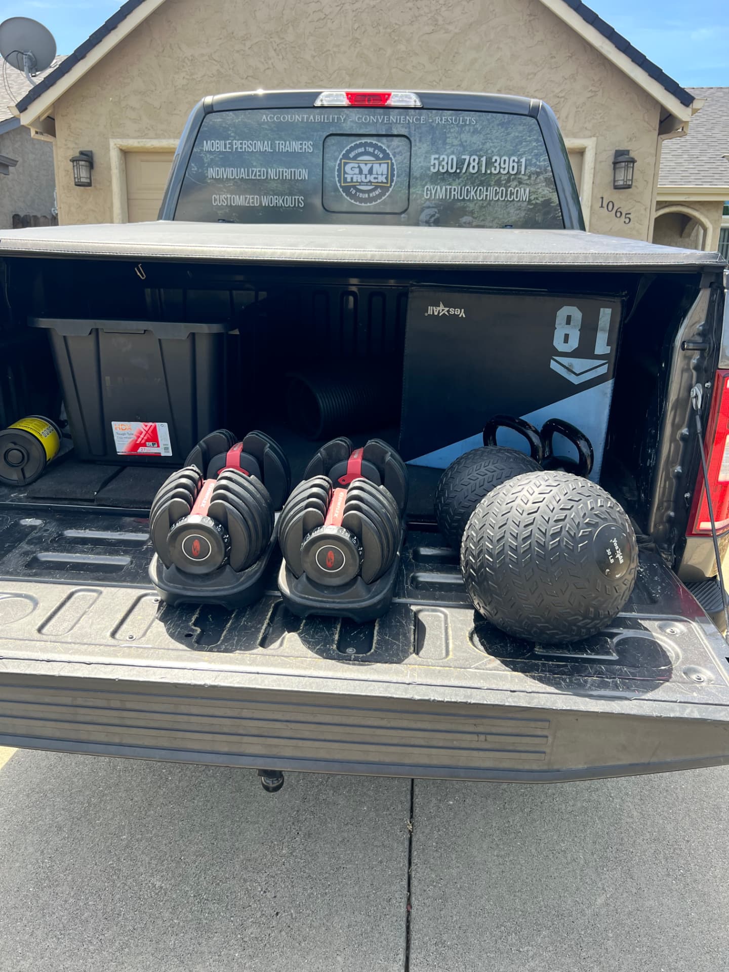 The open bed of the Gym Truck mobile personal training vehicle shows adjustable dumbbells, kettlebells, resistance bands, and portable workout equipment, ready to bring a complete gym experience to any home in Chico, CA.