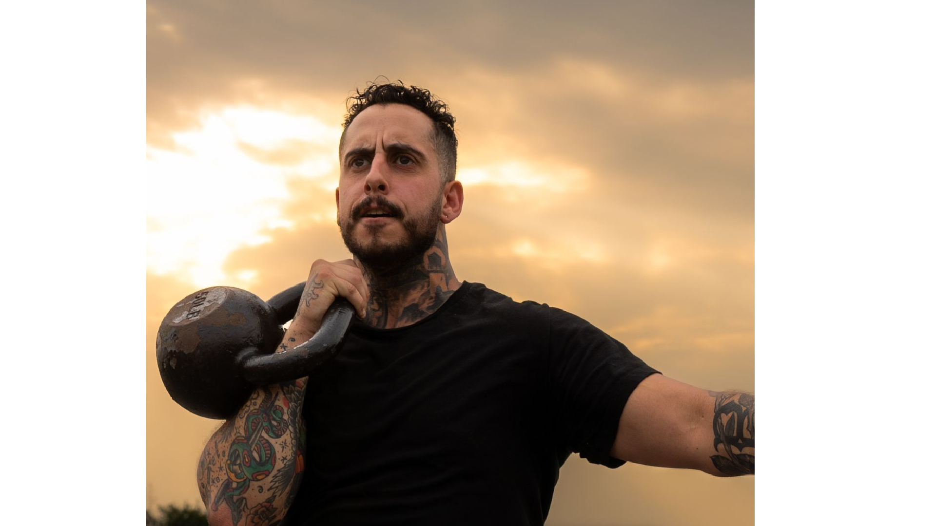 A certified personal trainer with tattooed arms performs a single-arm kettlebell lift at sunset, showcasing the strength and conditioning focus of fully customized private sessions with Gym Truck Chico in Chico, CA.