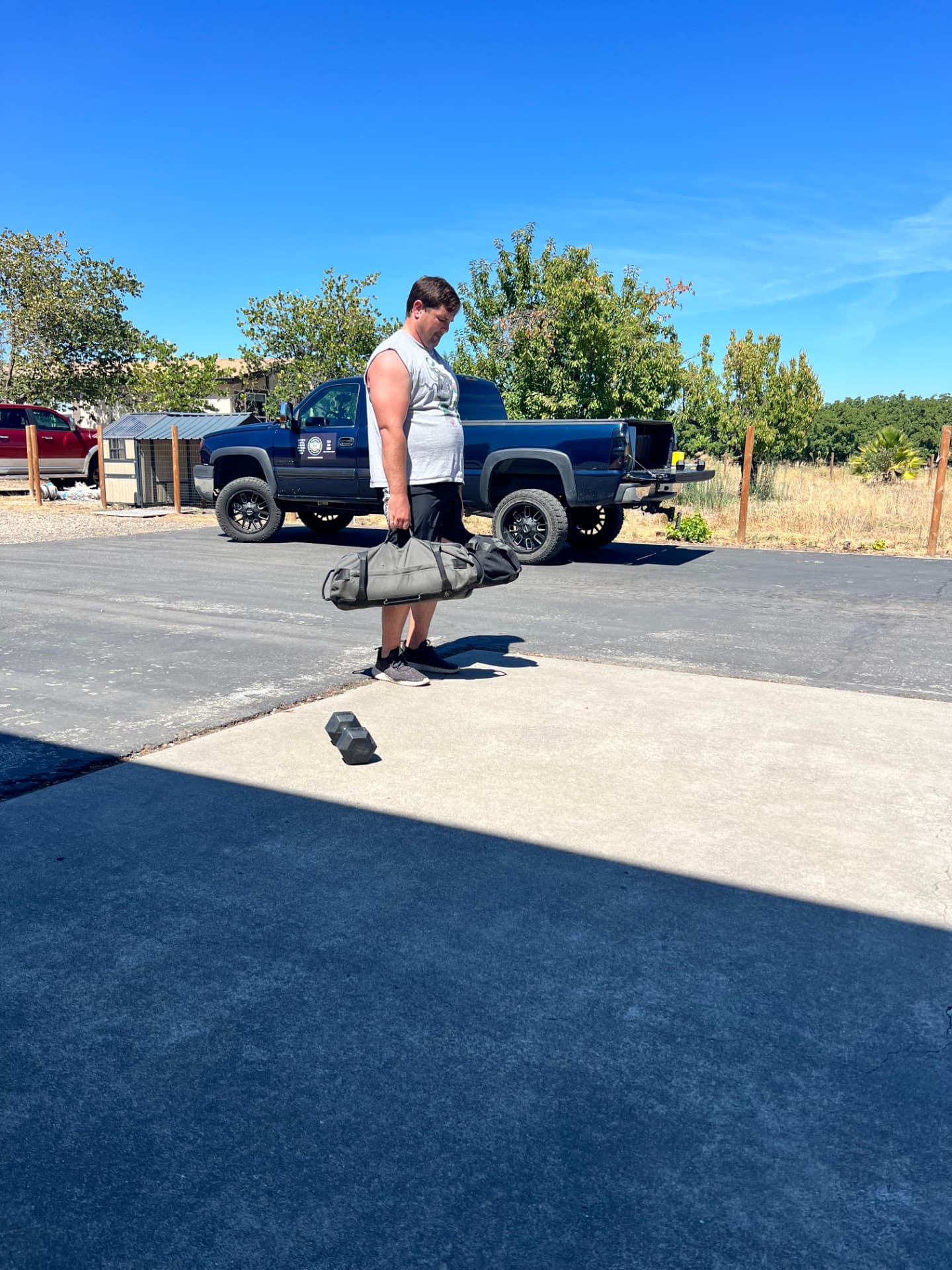 A man performs a double sandbag deadlift outdoors in front of the Gym Truck Chico mobile training vehicle, demonstrating effective, fully customized weight-loss and fat-burning strength training in Chico, CA.
